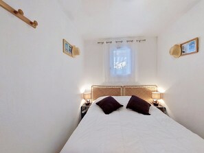 A bedroom with a bed, two bedside lamps, a window with a view, and a wooden headboard. - Les Jardins de l'Océan by Interhome (Vaux Sur Mer)