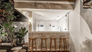 Eine Bar mit Sitzhocker, einer Betonwand und Blick in einen Raum mit weißer Decke und einer Tür.