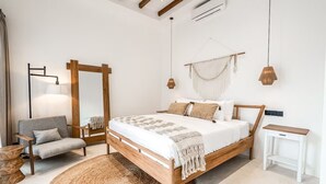 Ein Schlafzimmer mit einem hölzernen Bett, einem grauen Sofa, einem runden Teppich aus Gewebe und einer Wanddekoration aus Makramee.