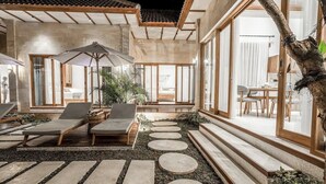Eine moderne Außenpatio mit Lounge-Möbeln, einer Holzpergola und einem Steinweg, der zu einer Glastür führt.