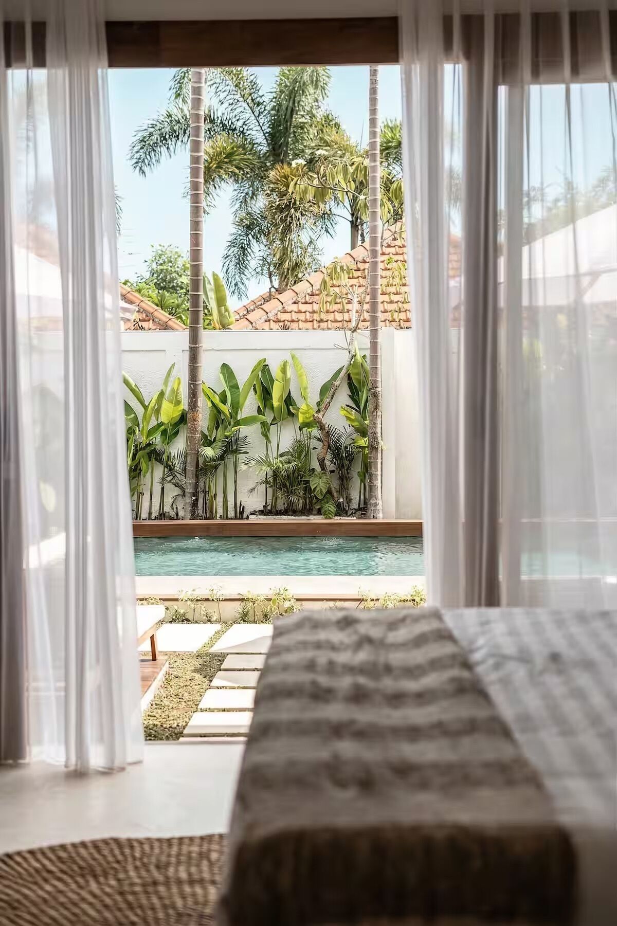 Ein Schlafzimmer mit Blick auf einen Pool und tropische Pflanzen.