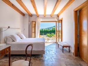 A bedroom with a bed, a chair, a wooden bench, and a view of a balcony with outdoor furniture. - Villa mit Jacuzzi by Interhome (Selva)
