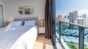 Ein modernes Hotelzimmer mit einem großen Bett, einem Nachttisch mit Lampe, einem Spiegel und einem Balkon mit Blick auf die Stadt.
