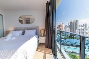 Ein modernes Hotelzimmer mit einem großen Bett, einem Nachttisch mit Lampe, einem Spiegel und einem Balkon mit Blick auf die Stadt.