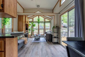 A spacious living area with a kitchen, large windows, and a view of the outdoors. - The Nook Tiny Home Fire Pit Close to Lake (Eagle Lake)