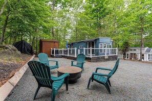 Ein überdachter Außenbereich mit Adirondack-Stühlen und einem runden Tisch, umgeben von einer Kiesfläche.