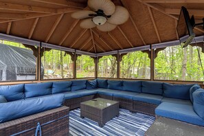 Ein überdachter Außenbereich mit einer großen Eckcouch, einem Couchtisch in der Mitte und einem Deckenventilator.