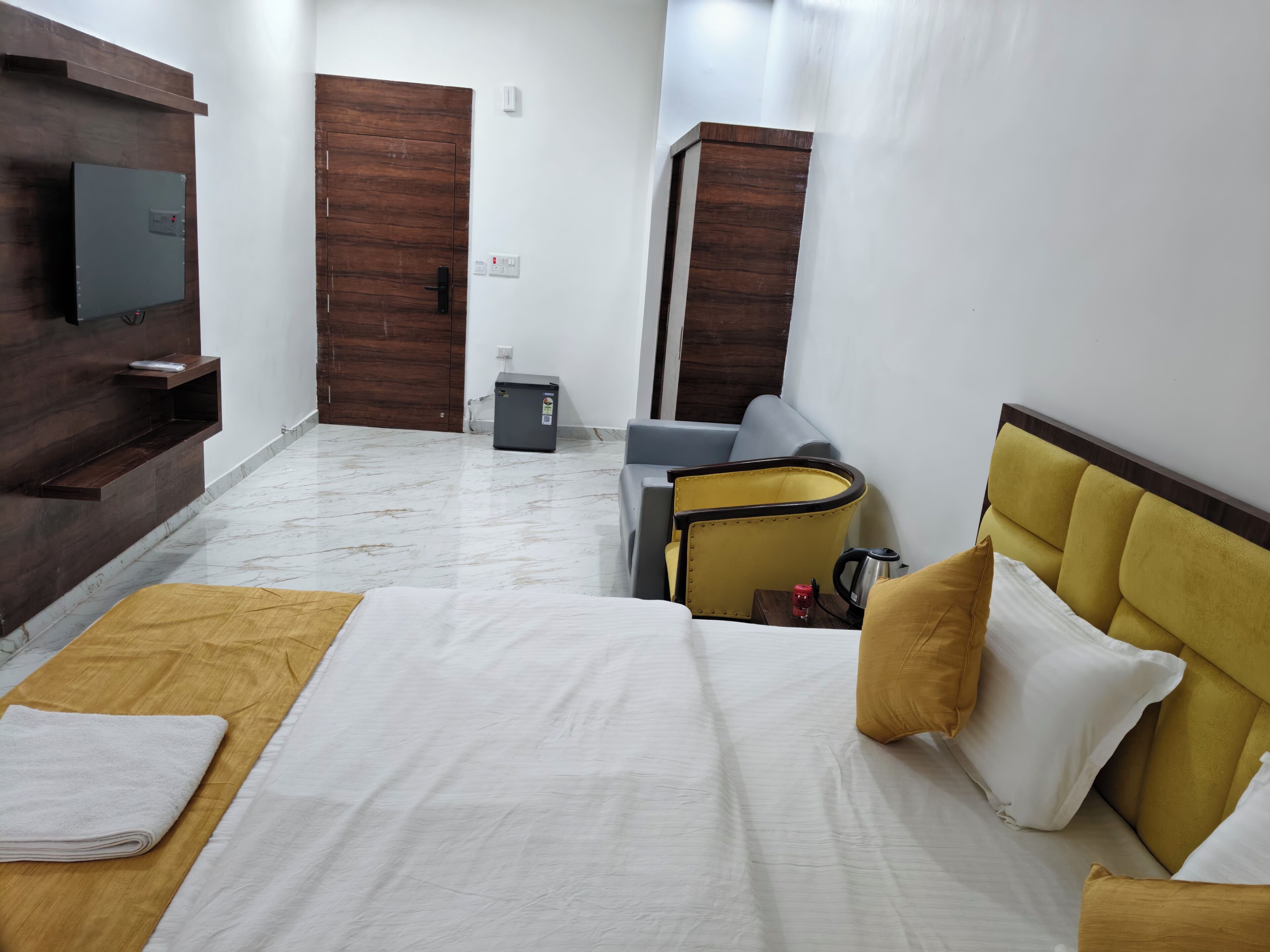 A hotel room with a bed, a TV, a small refrigerator, a seating area with a chair, and a wooden wall unit.