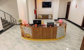 A reception desk with a marble floor, a television above it, and a staircase to the left.