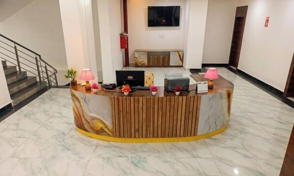 A reception desk with a marble floor, a staircase to the left, and a flat-screen TV mounted on the wall.