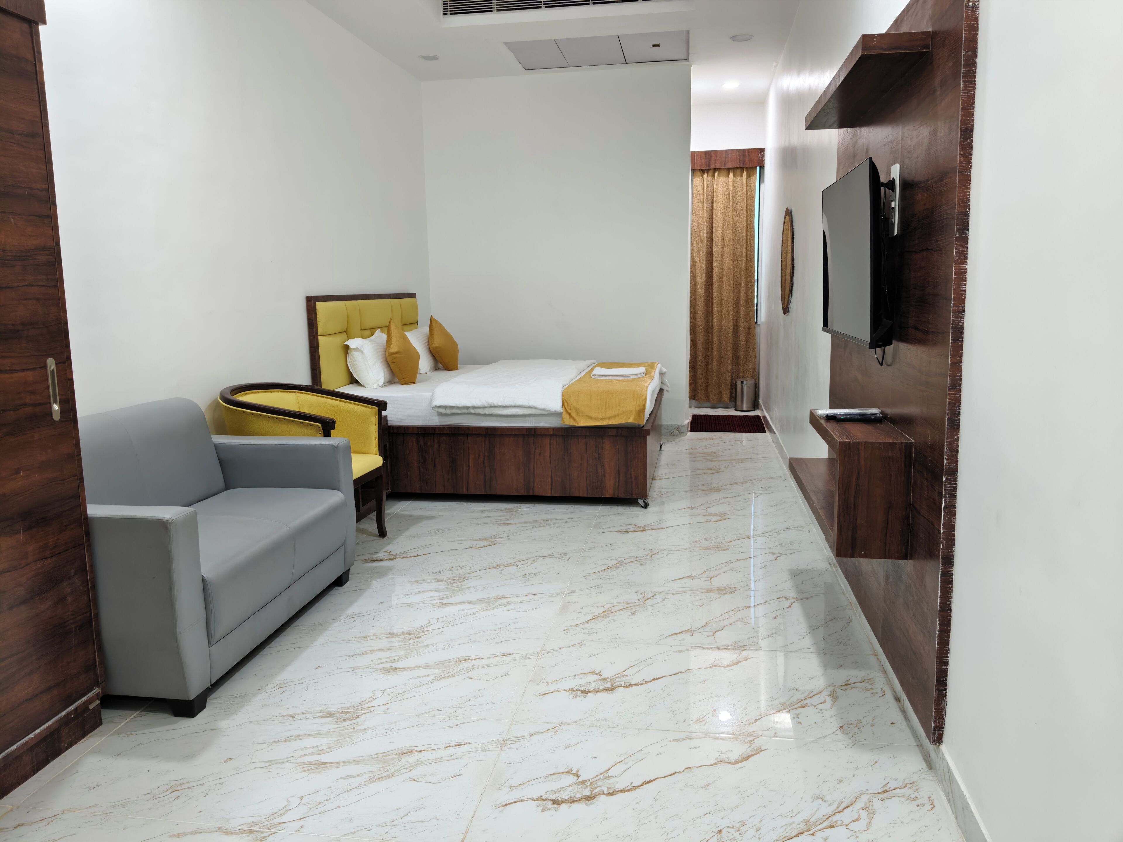 A hotel room with a bed, a sofa, a television, and a marble floor.