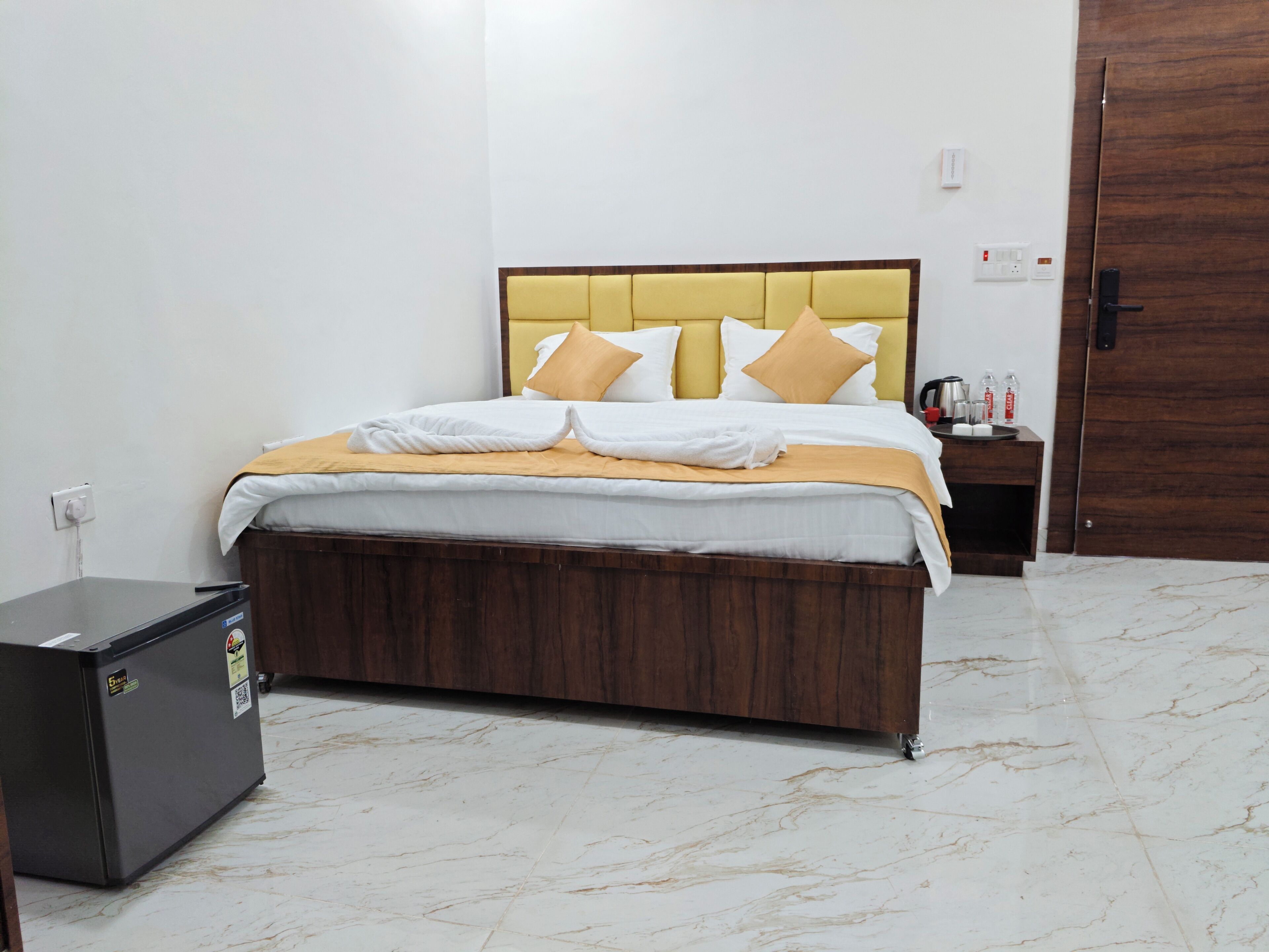 A hotel room with a bed, a wooden nightstand, a black cabinet, and a marble floor.