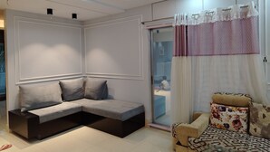 Una sala de estar moderna con un sofá modular, un sillón estampado y un ventanal de vidrio que da a un balcón.