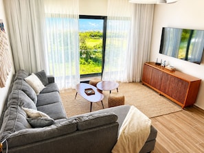 Ein modernes Wohnzimmer mit einem grauen Sofa, zwei runden Tischen, einer Holzkommode und einem großen Fernseher.