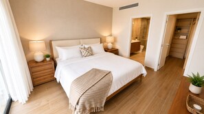 Ein Schlafzimmer mit Bett, Nachttischen, einer Lampe, einer Pflanze und einem durchgegangenen Tür sichtbaren Badezimmer.
