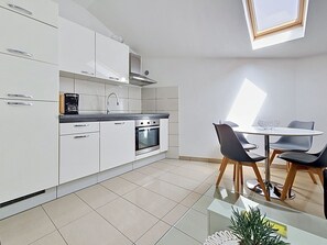 A modern kitchen with white cabinets, a coffee machine, and an oven. There is a dining area with a glass table and black chairs. - Mary & Klara by Interhome (Trogir/Okrug Gornji)