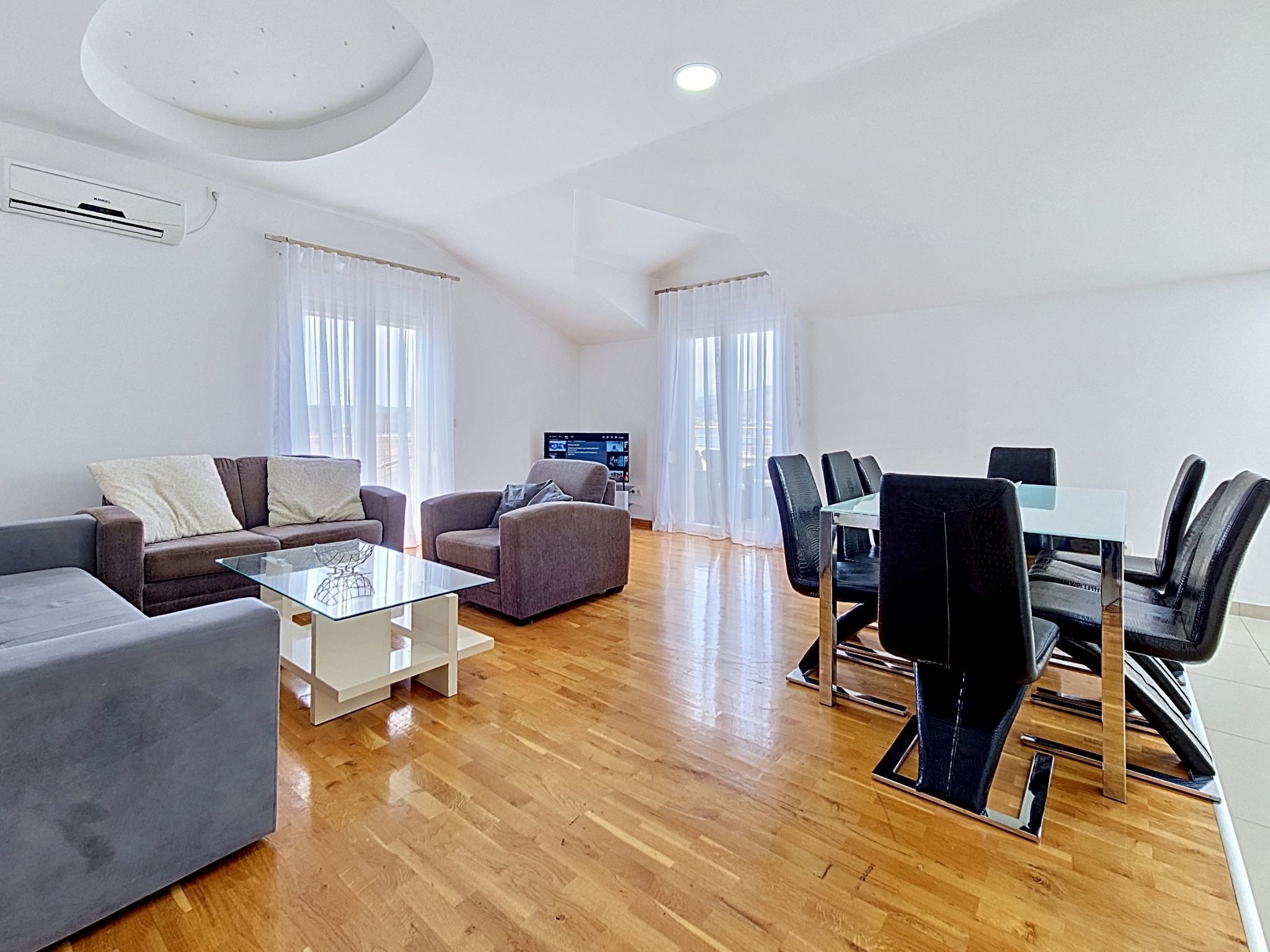Uma sala de estar moderna com sofá, poltronas, mesa de centro de vidro e um espaço de refeições com cadeiras e mesa.