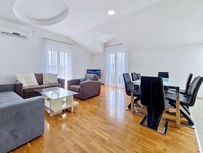 Een moderne woonkamer met een bank, fauteuils, een glazen salontafel en een eethoek met stoelen en een tafel.