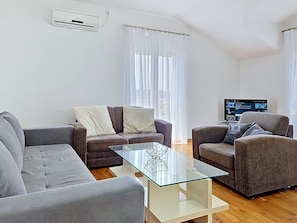 Ein modernes Wohnzimmer mit einem Glastisch, zwei Sofas, einem Fernseher und einer Klimaanlage.