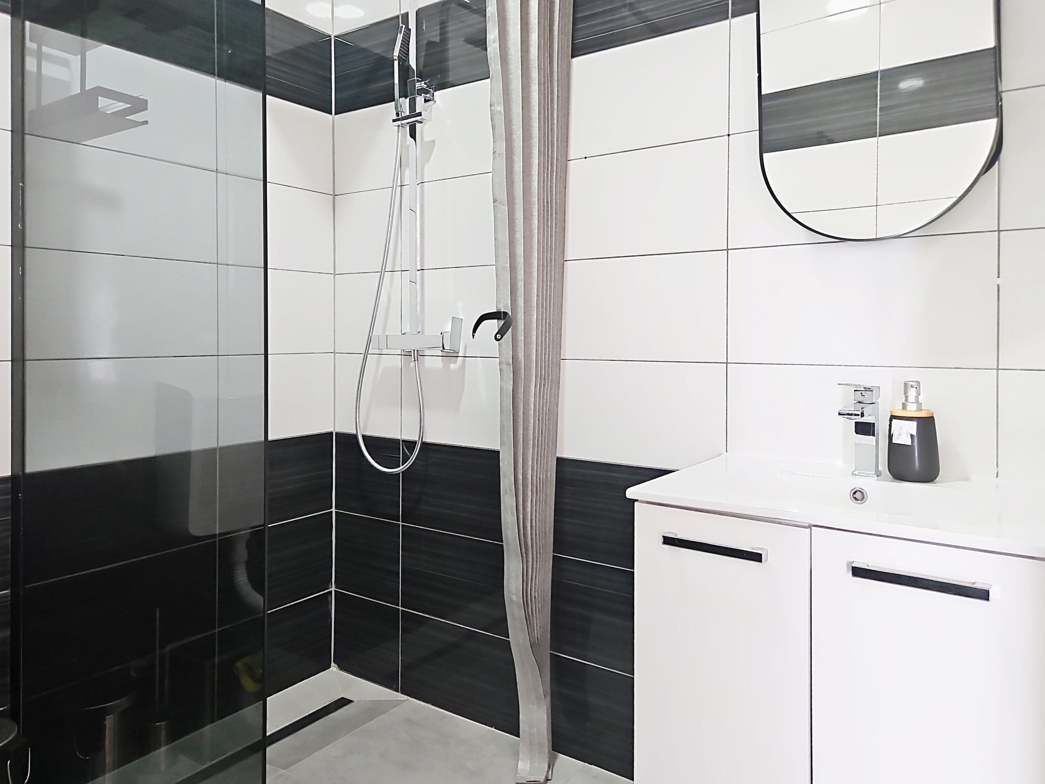 A modern bathroom with a shower, a mirror, and a sink with a soap dispenser.