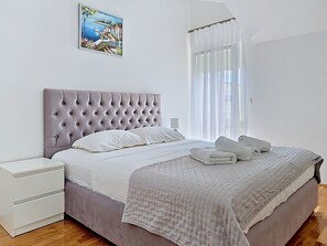 Ein Schlafzimmer mit einer karottenförmigen Kopfteile, einem Bett mit weißen Bettwäsche, einem Nachttisch, einem aufgerollten Handtuch und einem Bild an der Wand.