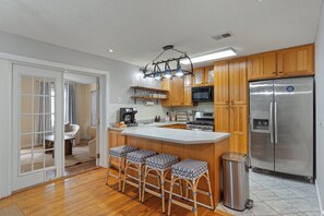 A modern kitchen with wooden cabinets, a stainless steel refrigerator, and a bar area with stools. - NEW! Okaloosa Island, Destin, Navarre
3 bedroom/ 2 bath, pool, beach gear (Mary Esther)
