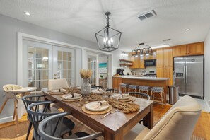 A dining area with a wooden table set for six, surrounded by chairs, a chandelier, and a kitchen in the background. - NEW! Okaloosa Island, Destin, Navarre
3 bedroom/ 2 bath, pool, beach gear (Mary Esther)