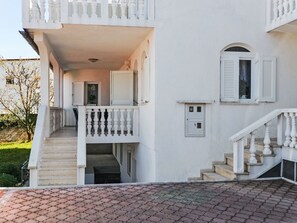 Ein zweistöckiges Gebäude mit Balkon, Treppe und einer kleinen Tür mit Rollläden.
