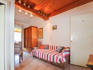 Ein Zimmer mit Holzbalkendecke, einem Bett mit gestreifter Bettwäsche, einem Holzschrank und einer Tür mit einer Nummer.
