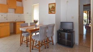 A dining area with a wooden table and chairs, a kitchen with wooden cabinets, a painting on the wall, and a TV stand. - Apartment Jako by Interhome (Trogir/Slatine)