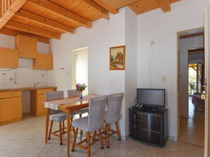 Ein Essbereich mit Holztisch und -stühlen, eine Küche mit Holzschränken, ein Gemälde an der Wand und ein TV-Möbel.