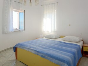 Ein Schlafzimmer mit Bett, Vorhängen, einem Fenster und einem Nachttisch.