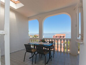Ein Balkon mit Tisch und Stühlen, Blick auf Gebäude und ein Gewässer, dazu ein klarer Himmel.