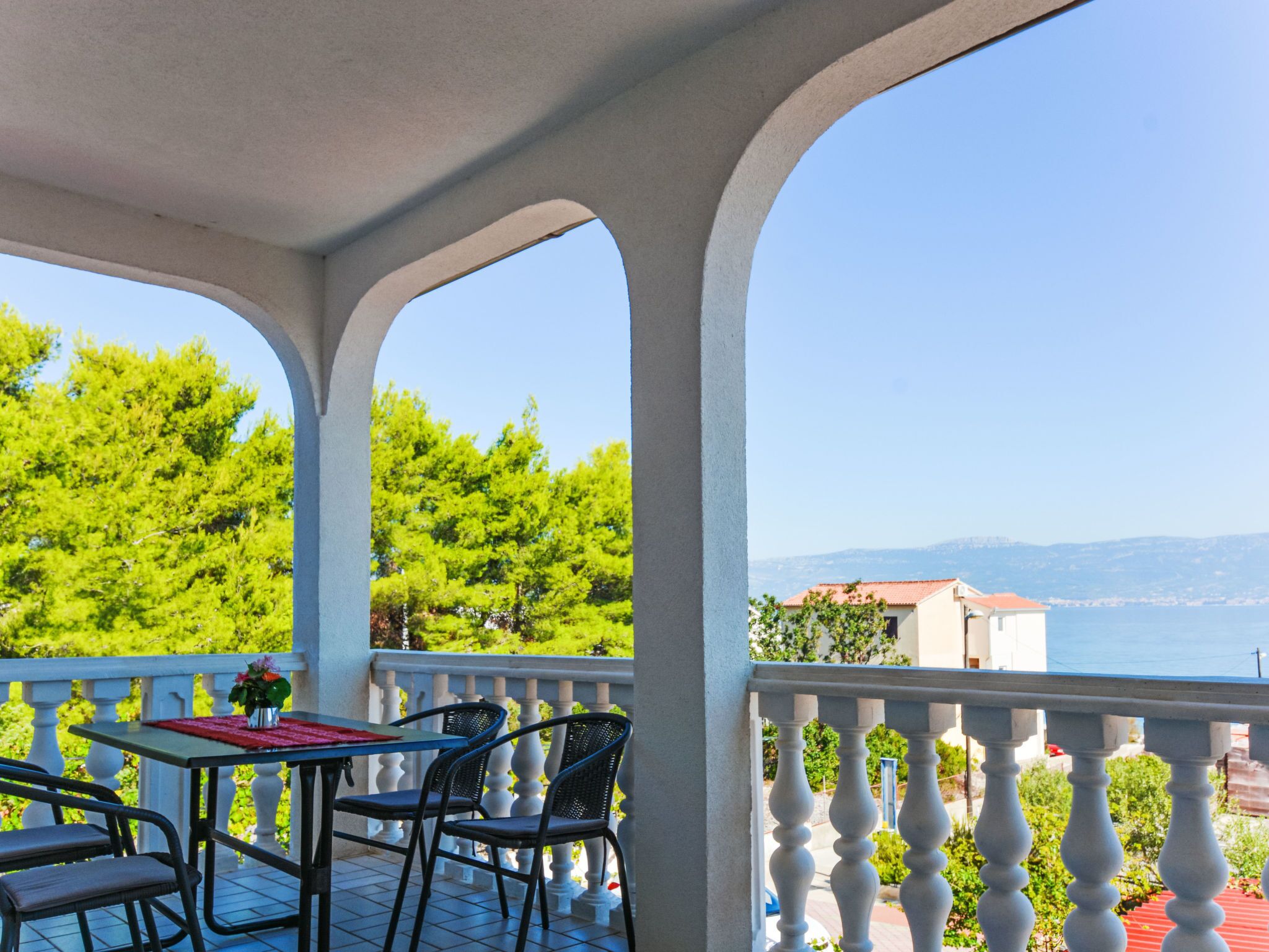 A balcony with a table and chairs, overlooking a coastal landscape with trees and buildings.