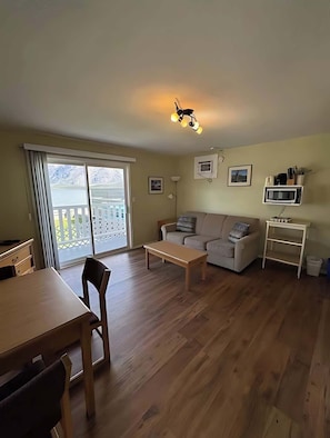 Un salon comprenant un canapé, une table basse, une table à manger et des chaises. Il y a un balcon avec vue sur les montagnes.