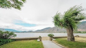 A lakeside view with a concrete pathway, a tree, and a distant mountain range. - 1 BR Suite 9 at Green Gables Resort (Osoyoos)