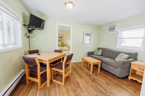 Ein Zimmer mit Esstisch, Stühlen, einer Couch, einem an der Wand befestigten Fernseher und einem Fenster.