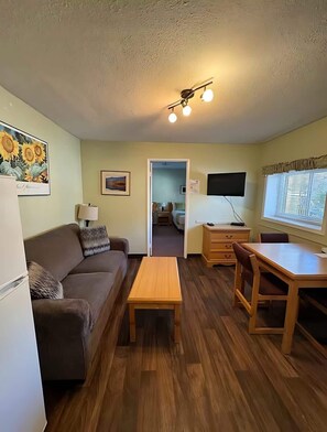 Un espacio habitable pequeño con un sofá, una mesa de madera, un televisor y una puerta que da a un dormitorio.
