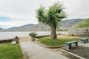A lakeside park with a tree, benches, and a concrete walkway.