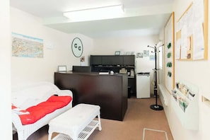 A compact room with a bed, a desk, a small kitchenette, and a bulletin board.