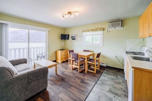 A cozy room with a sofa, a dining table with chairs, a TV, and a kitchen area with a stove and sink.