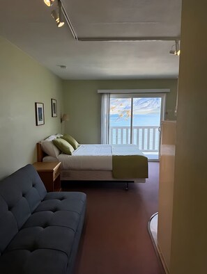 A bedroom with a bed, a nightstand, a sofa, and a large window with a view of the sea.