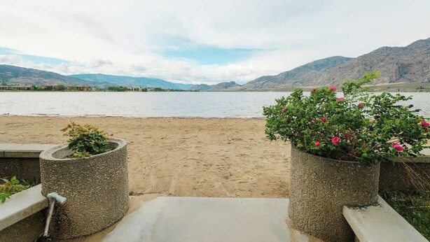 Vista de playa con montañas al fondo, macetas de concreto con plantas y cielo despejado.