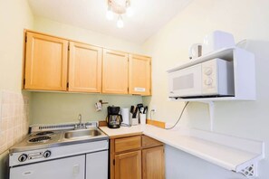 A compact kitchen with wooden cabinets, a stove, a microwave, and a coffee maker.
