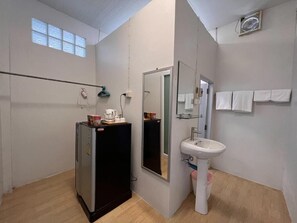 Un baño con lavamanos, espejo, toallero y un refrigerador pequeño.