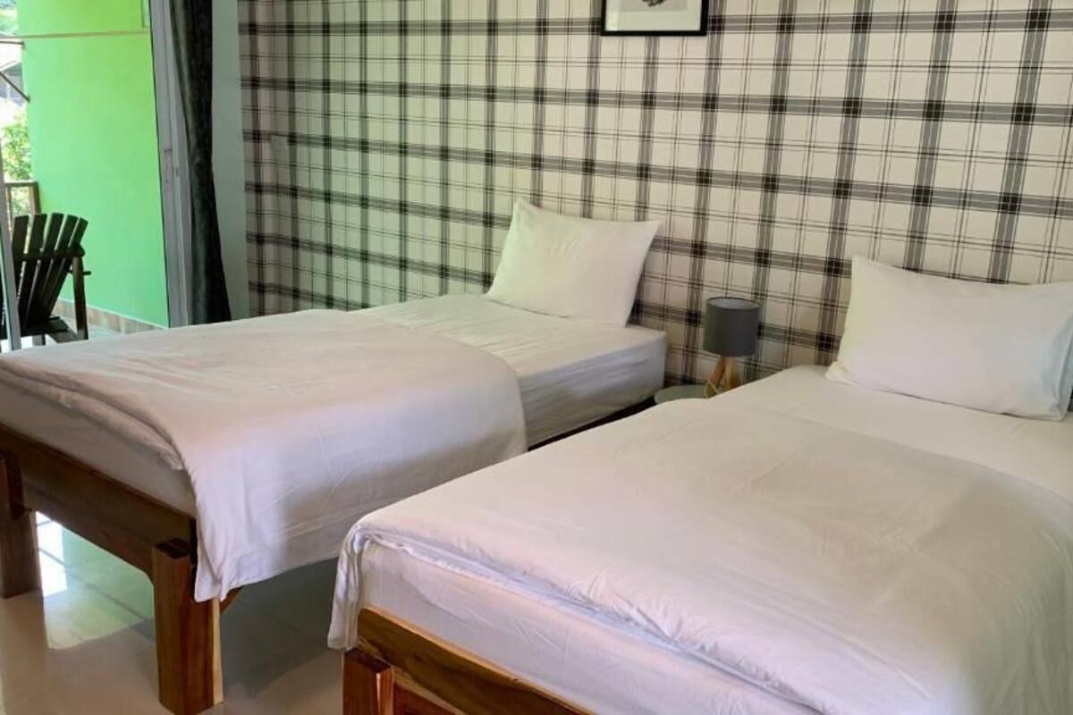 Dos camas individuales con sábanas blancas, un pared con estampado escocés y una puerta verde.