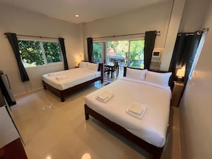 A hotel room with two beds, a dining area, and a view of greenery.