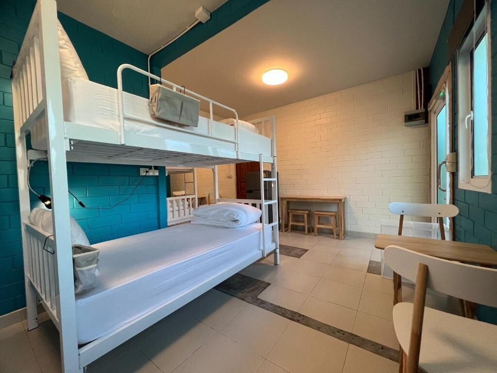 A bunk bed room with a desk and chair, white walls, and a window.