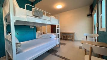 A bunk bed room with a desk and chair, white walls, and a window.