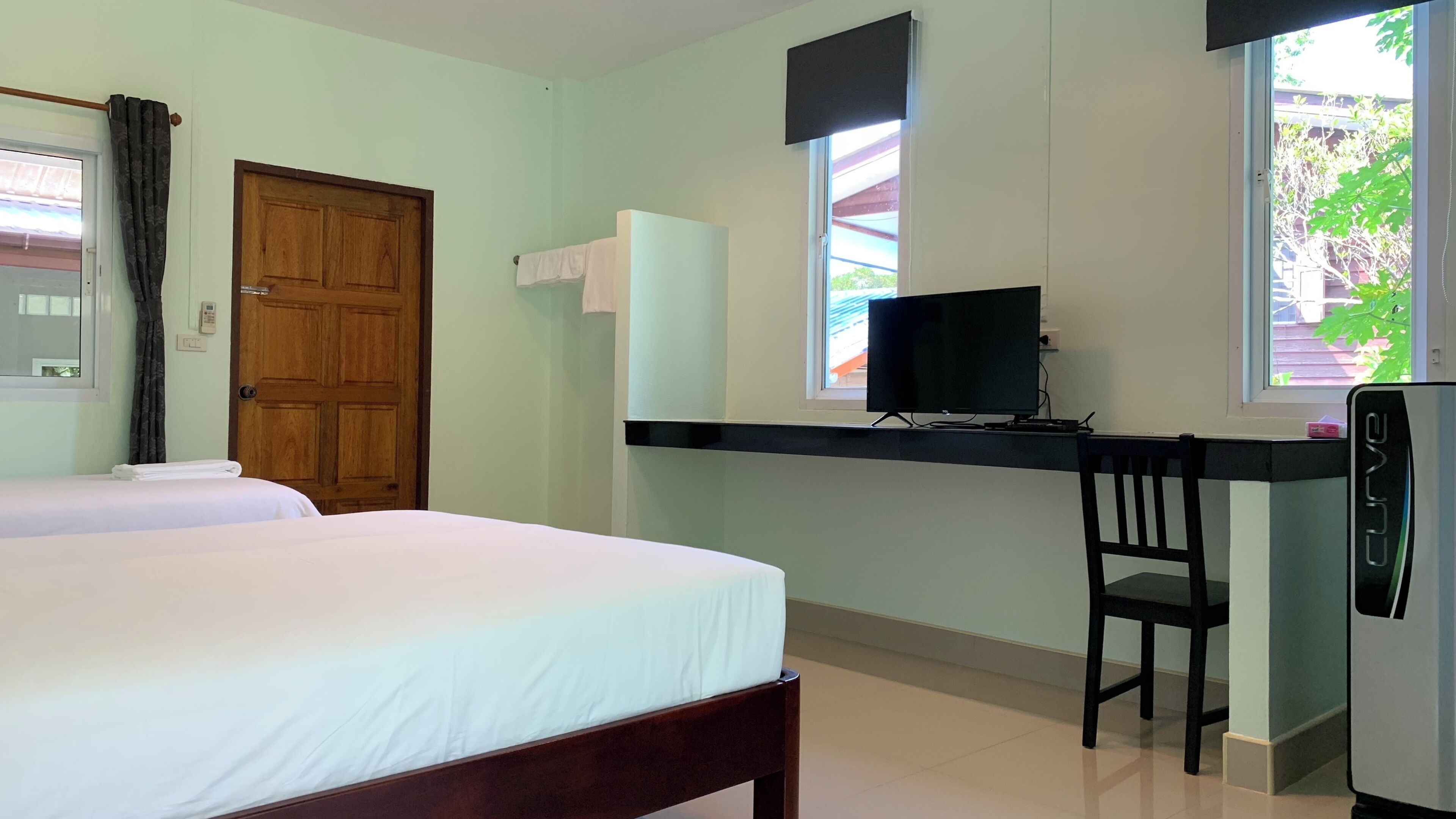 A hotel room with a bed, a desk with a computer, a chair, a TV, and a window.